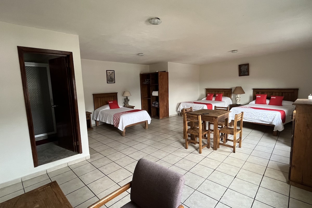 A hotel room with two beds, a dining table, and a chair. There is a wardrobe and a door leading to another room.