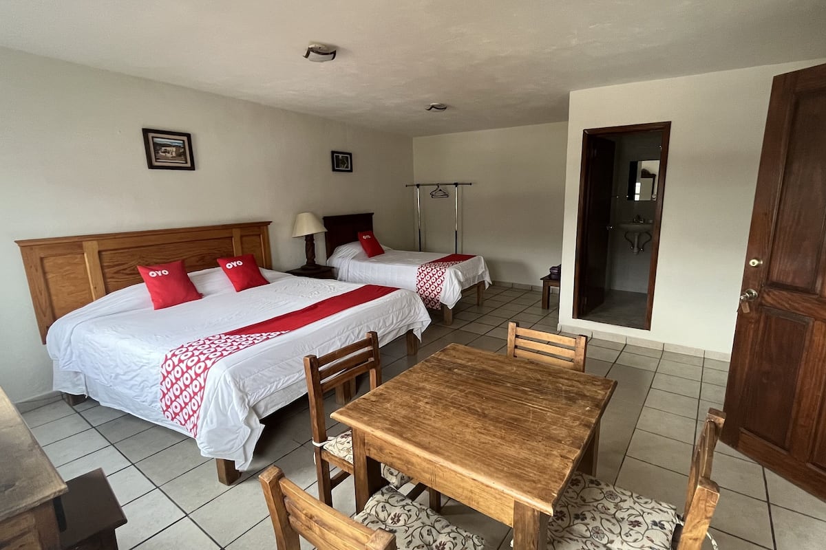 A hotel room with two beds, a wooden table, and a bathroom visible through an open door.