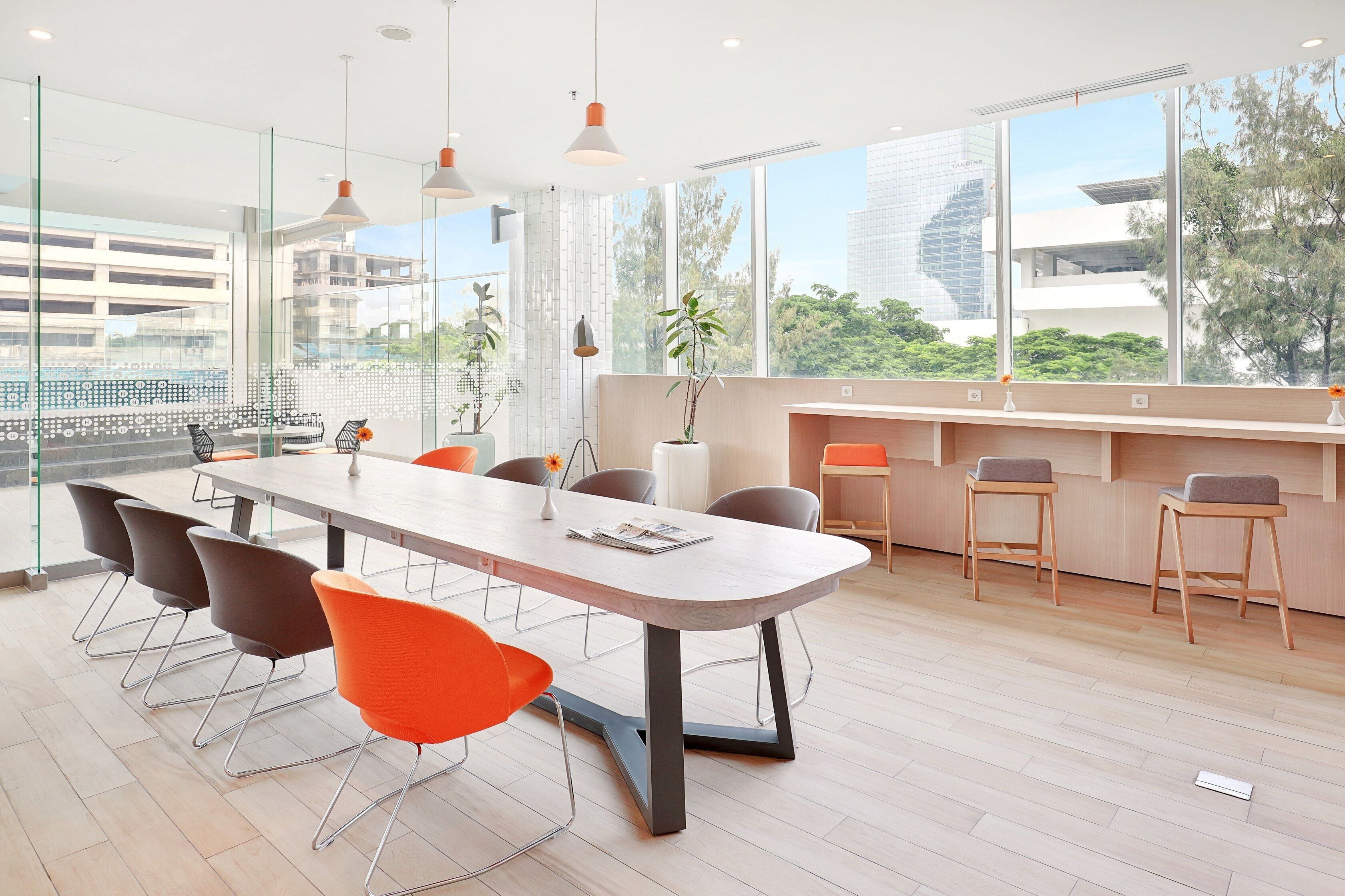 Une salle de conférence moderne, dotée d’une longue table, de chaises orange et d’une cloison en verre.