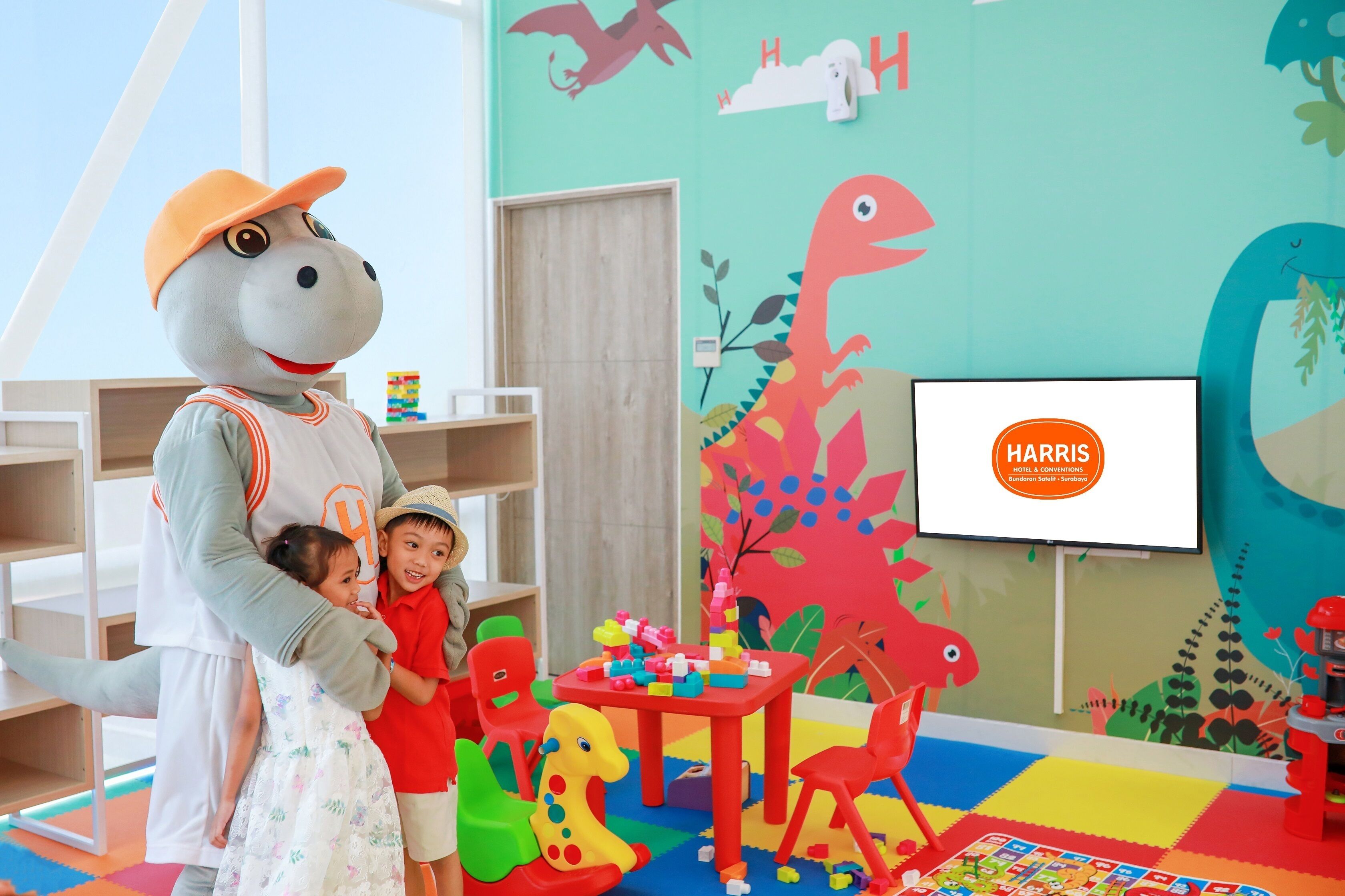A child interacting with a mascot in a colorful play area with dinosaur decorations and a Harris sign.