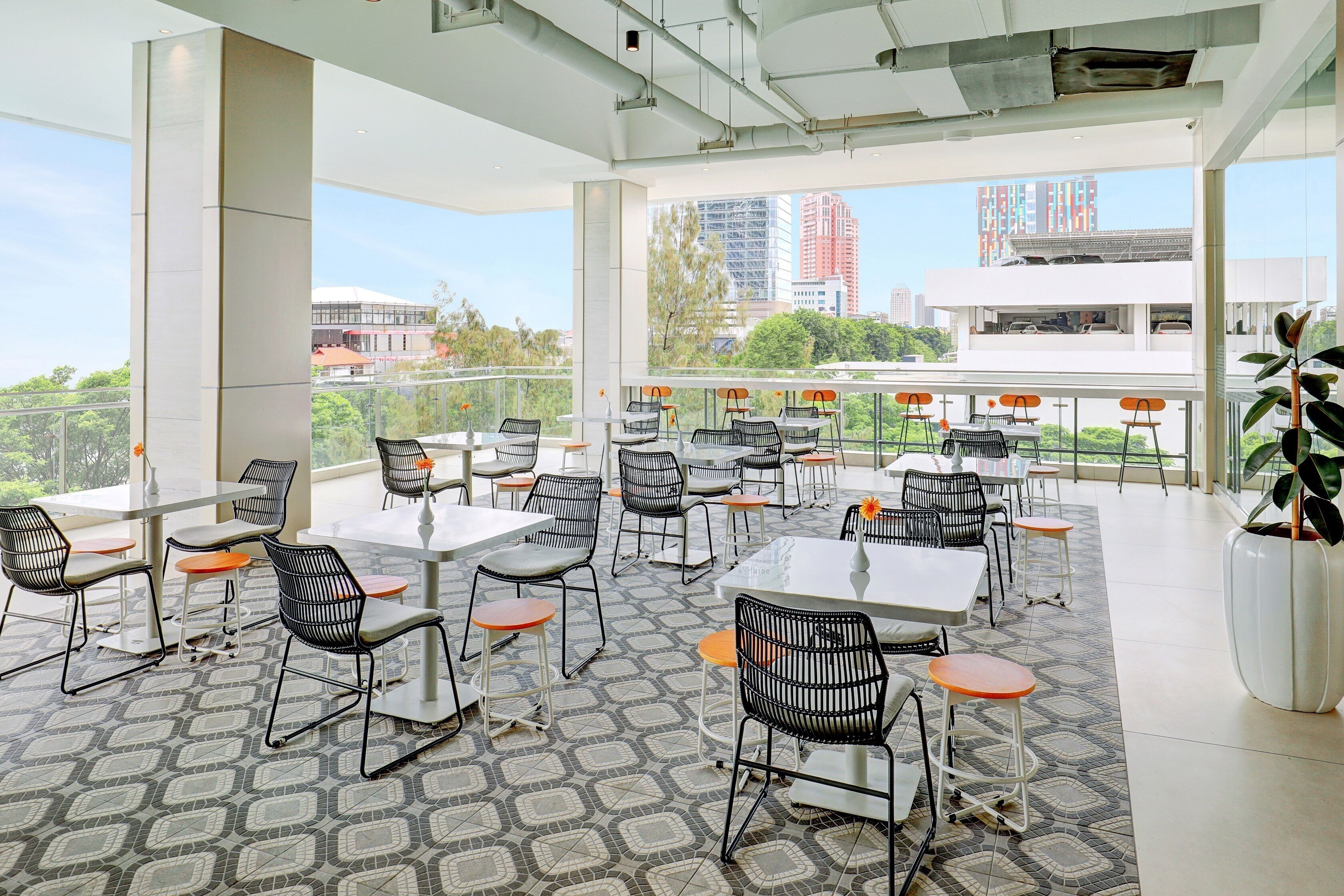 A modern outdoor dining area with tables and chairs, large windows offering city views, and a patterned floor.