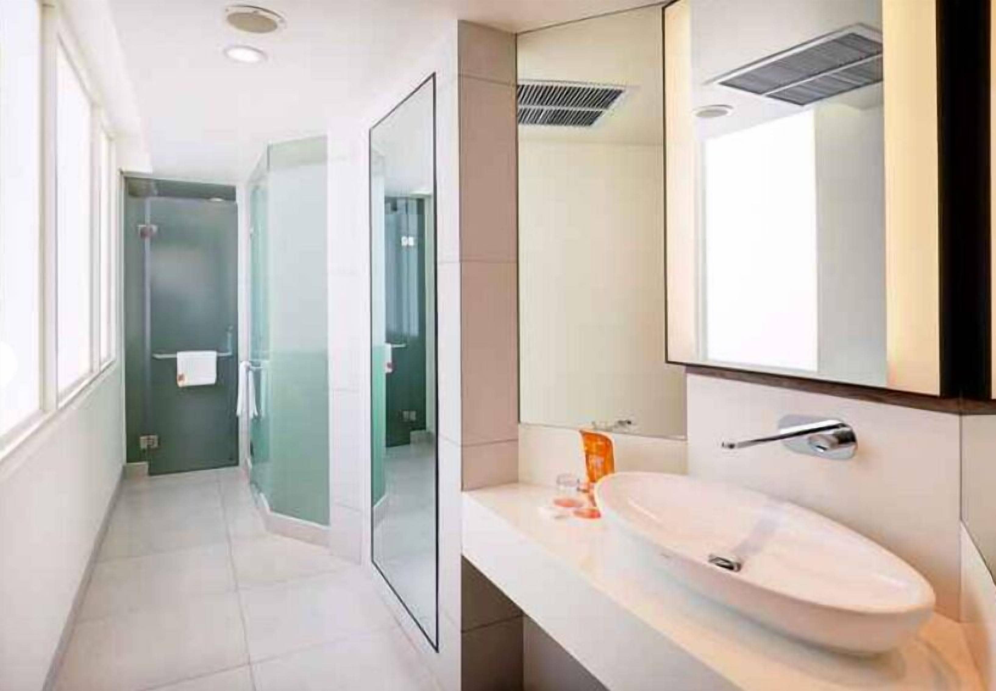 Une salle de bain moderne avec un lavabo blanc, un grand miroir et une douche à parois de verre.