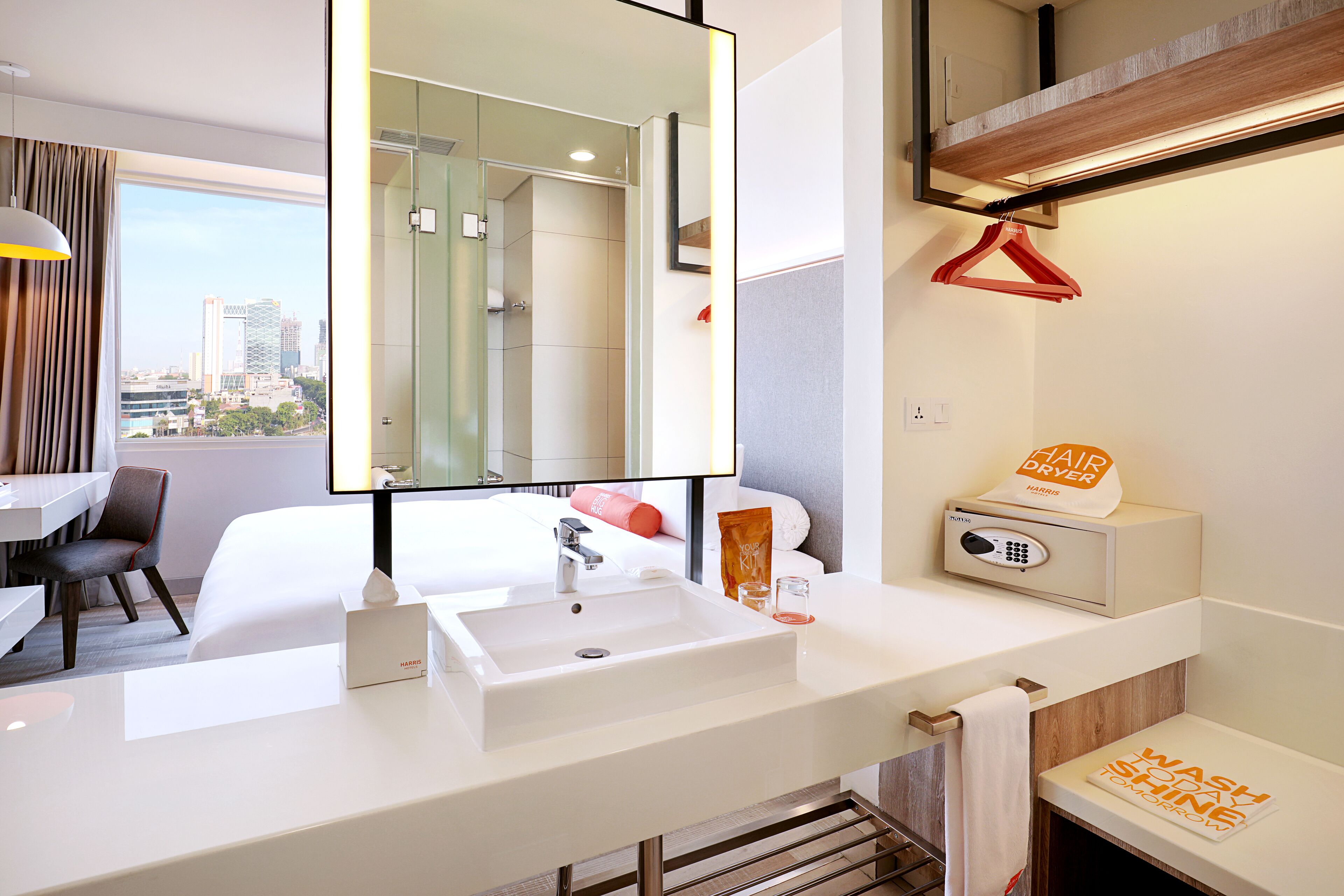 A modern hotel bathroom with a large mirror, a white sink, and a hair dryer.