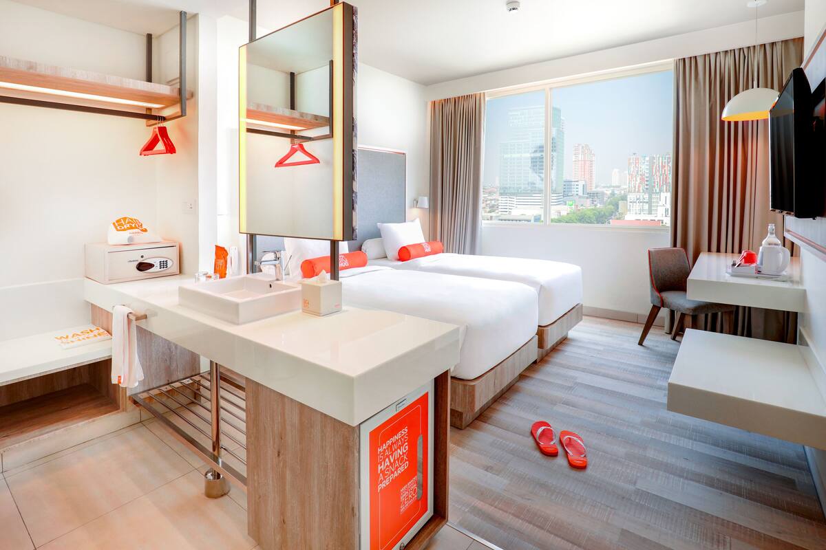 A hotel room with a large bed, a desk, a chair, a bathroom with a sink and mirror, and a city view.