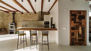 A modern kitchen with a central island, stone walls, exposed wooden beams, and a rustic wooden door.