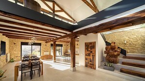 A spacious interior with exposed wooden beams, a stone wall, and a staircase with a unique wooden design.