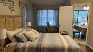 Una camera da letto con un letto, comodini, una sedia, un tavolo da pranzo con sedie e vista sull'esterno attraverso una finestra.