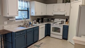 Una cucina con mobili bianchi e blu, un lavello in acciaio inossidabile, un forno a microonde, un forno e un frigorifero.