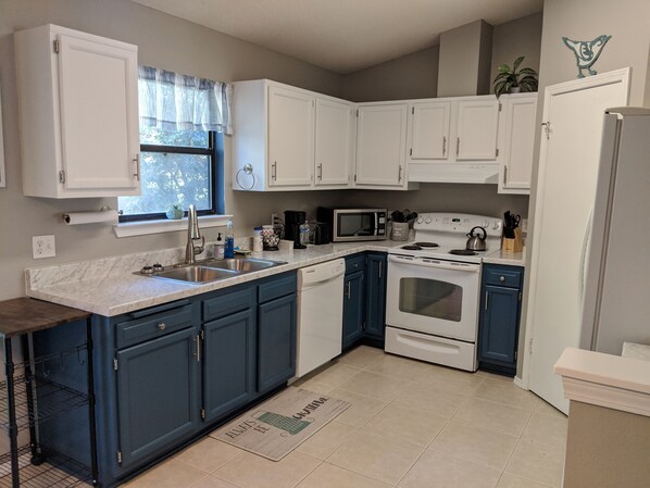 A kitchen with white and blue cabinets, a stainless steel sink, a microwave, an oven, and a refrigerator.
