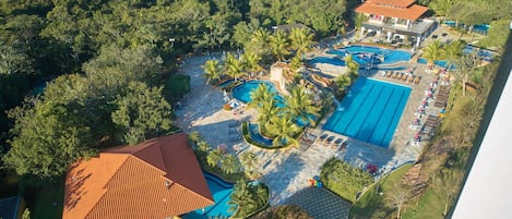 An aerial view of a resort with multiple swimming pools, palm trees, and a building with a red roof.