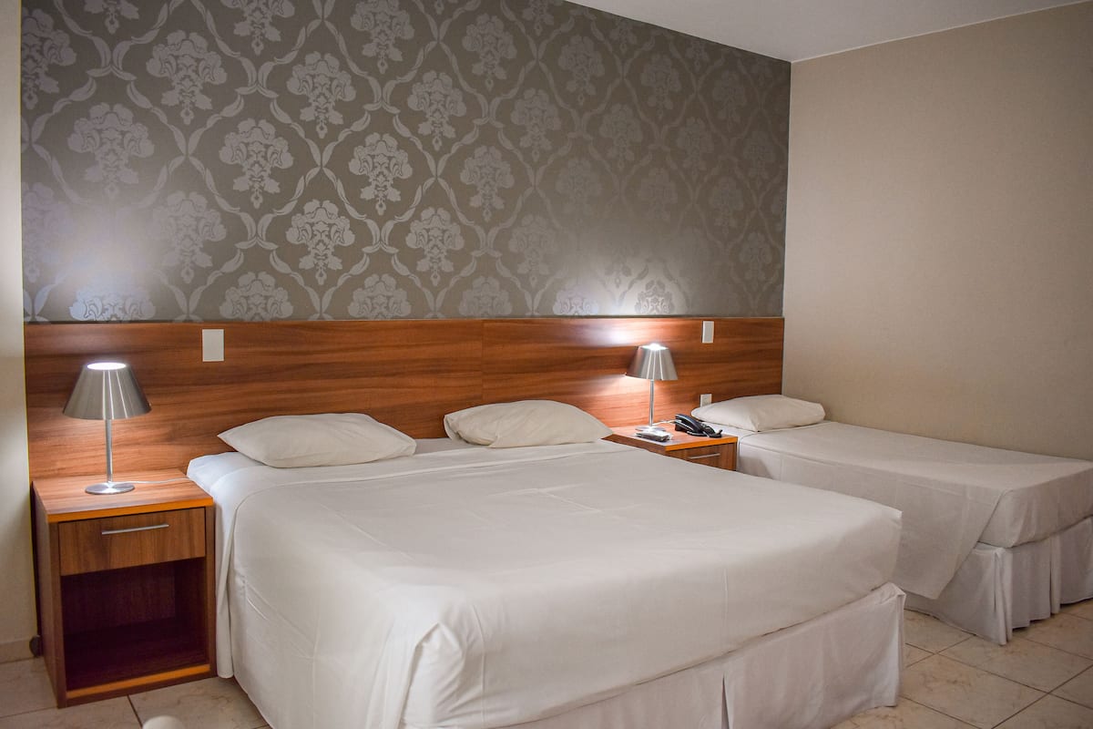 A hotel room with two beds, a wooden headboard, a nightstand with a lamp, and a patterned wallpaper.
