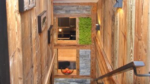 A wooden interior with a stone wall and a green wall. There are framed pictures on the walls and a basket with fruit.