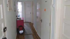 Un pasillo estrecho con puertas blancas, un escritorio rosa y una silla blanca.