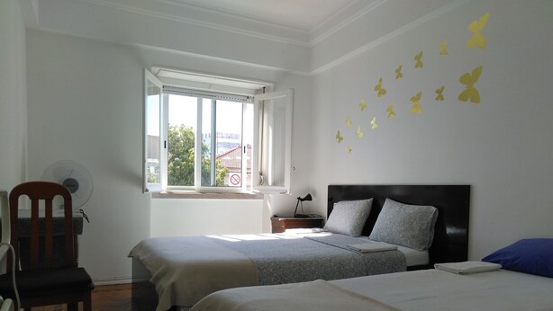 Habitación de hotel con dos camas, un escritorio, una silla, un ventanal con vistas y adhesivos decorativos de mariposas.