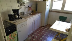 Una cocina compacta con gabinetes blancos, una estufa a gas, una cafetera y piso de baldosas.