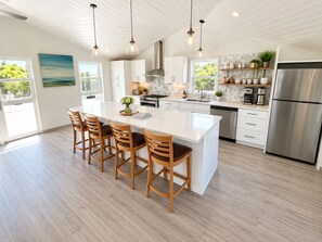 A modern kitchen with a large island, wooden bar stools, stainless steel appliances, and a view of greenery outside.