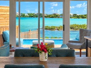 A room with a view of a turquoise sea and a wooden deck.