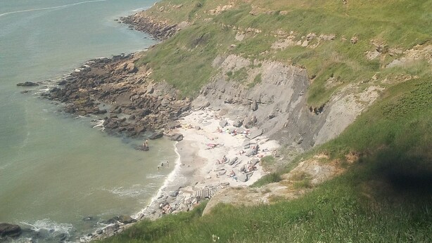 Een kustlandschap met een rotsachtig strand, grasheuvels en een heldere lucht.