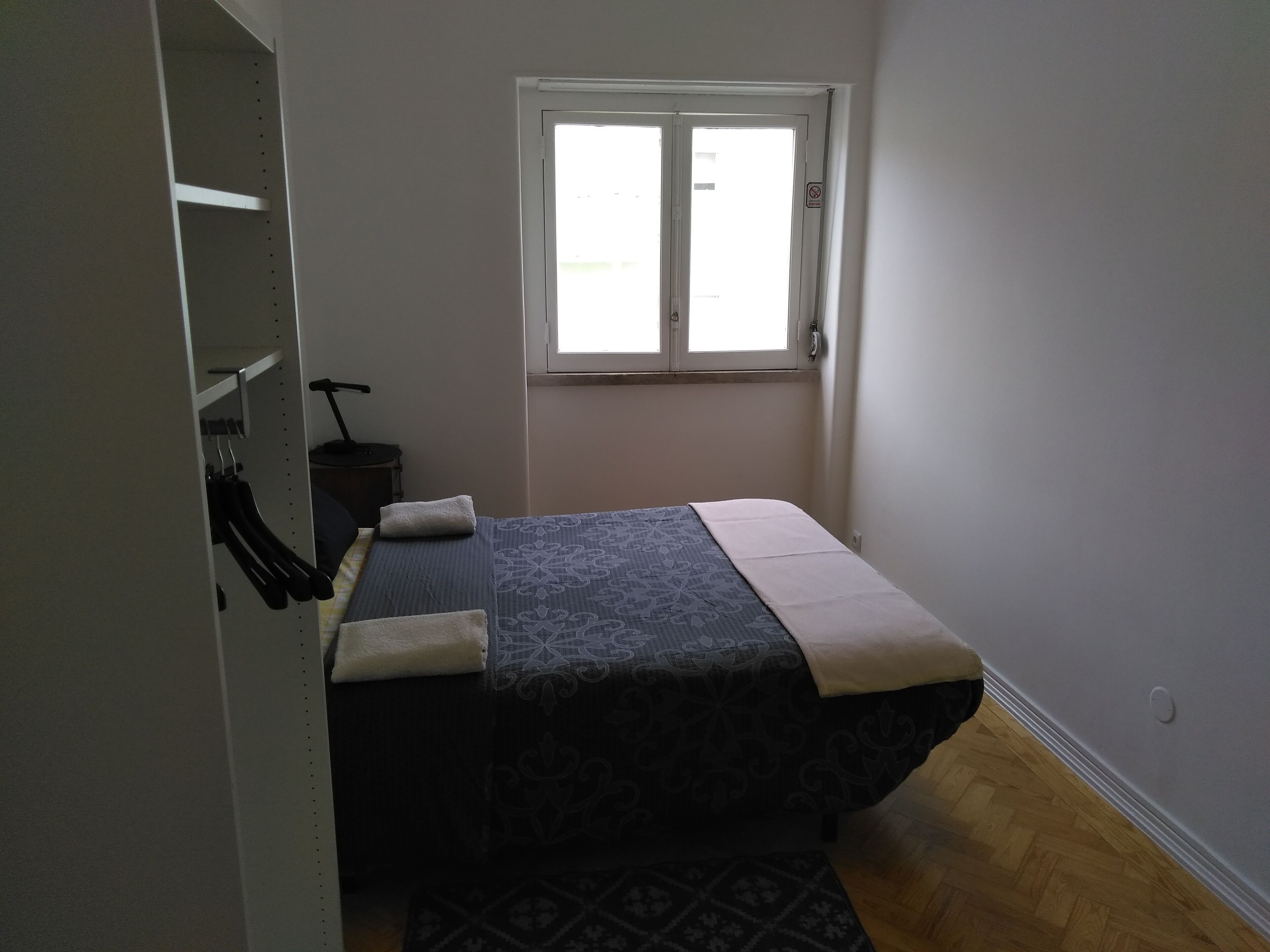 A small, narrow room with a bed, a window, and a wardrobe.