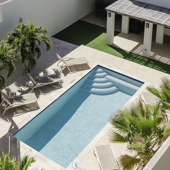 A rectangular swimming pool with a geometric pattern on the floor, surrounded by lounge chairs and palm trees.
