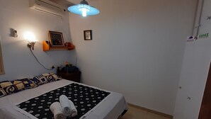 Un lit bien fait, recouvert d’une couvre-lit à motifs noir et blanc, une serviette enroulée posée sur le lit et un climatiseur fixé au mur.