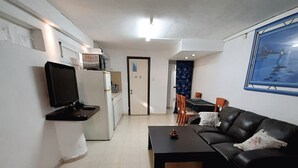 Un salon avec un canapé noir, une table basse, un téléviseur fixé au mur et un coin repas comprenant des chaises et une table.