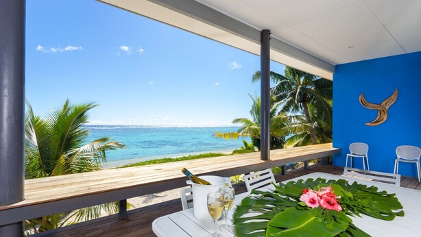 A table with a bottle of champagne, two glasses, and a tropical leaf arrangement on a balcony overlooking the sea. - Panama Beachfront Apartments Rarotonga (Rarotonga)