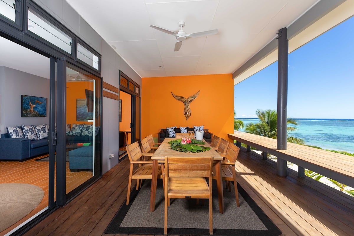 A dining area with a wooden table and chairs, a ceiling fan, and a view of the ocean.