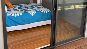 A bedroom with a bed, a sliding glass door leading to a balcony, and a painting on the wall. - Panama Beachfront Apartments Rarotonga (Rarotonga)