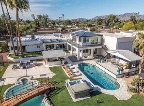 A modern multi-story house with a swimming pool, outdoor seating, and a view of mountains. - Luxury Scottsdale Home:6BR W/8 Beds, 4BA,Heated Pool, HotTub,Putting Green,&More (Scottsdale)