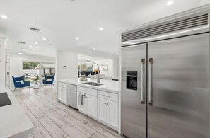 A modern kitchen with white cabinetry, a stainless steel refrigerator, and a dining area with blue chairs. - Luxury Scottsdale Home:6BR W/8 Beds, 4BA,Heated Pool, HotTub,Putting Green,&More (Scottsdale)