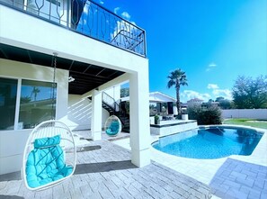 Une maison moderne à deux étages, dotée d’une piscine, d’un espace extérieur aménagé et surplombée d’un ciel d’un bleu éclatant.