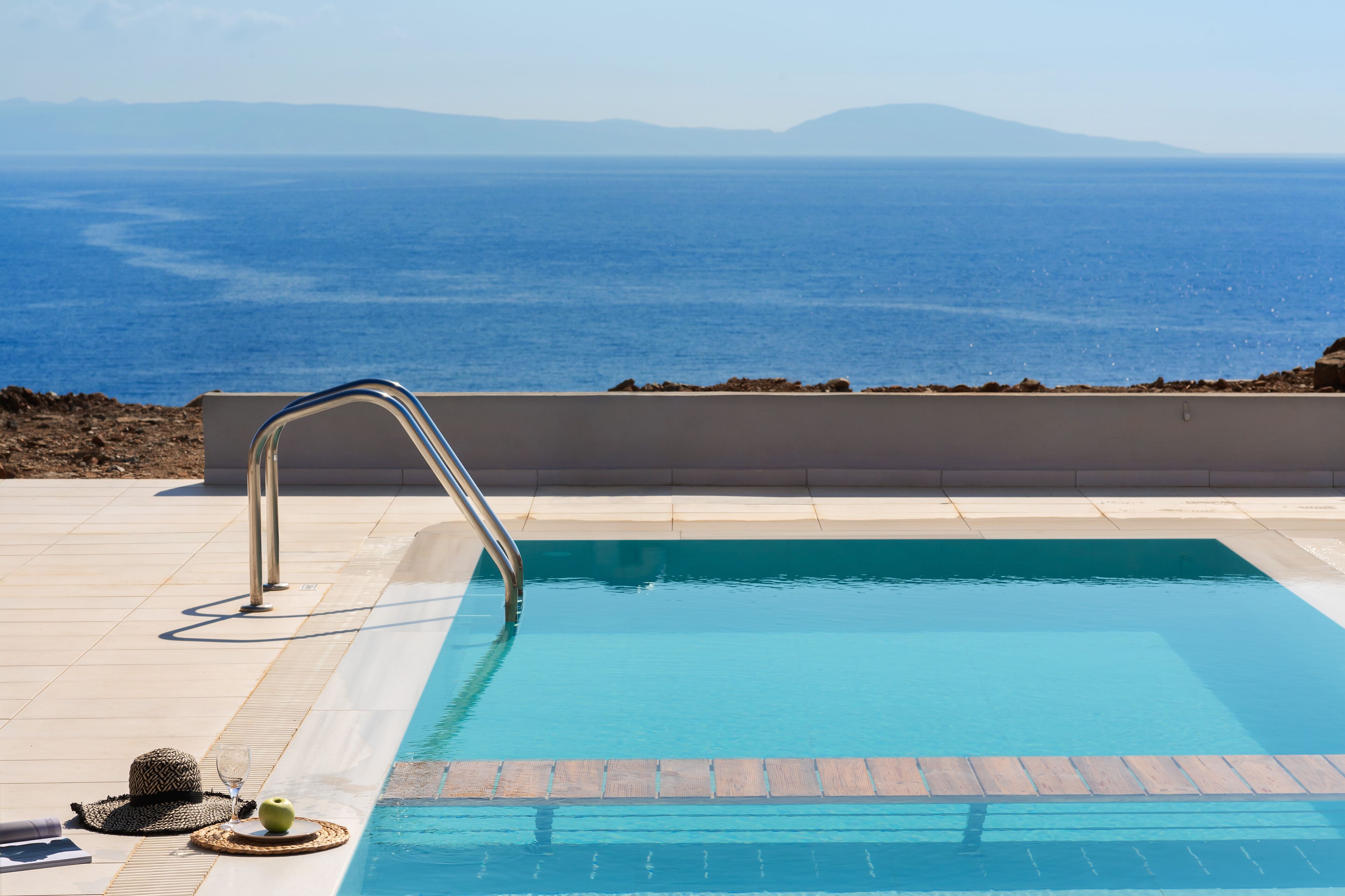 A pool with a metal ladder, a hat, and a glass of water on the edge.