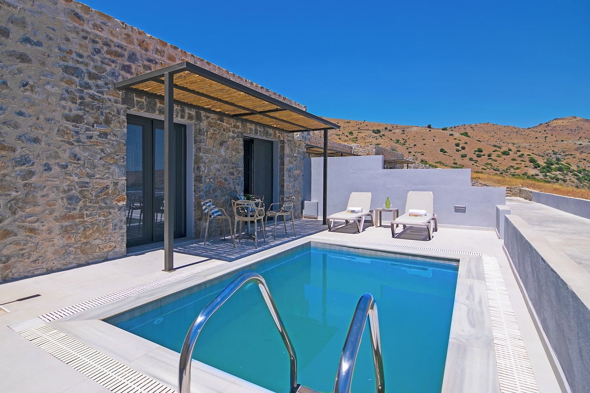 Edificio de piedra con piscina, zona de estar al aire libre y vistas a colinas.