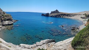 Un paysage côtier caractérisé par un terrain rocheux, une mer d’un bleu limpide et une petite plage.
