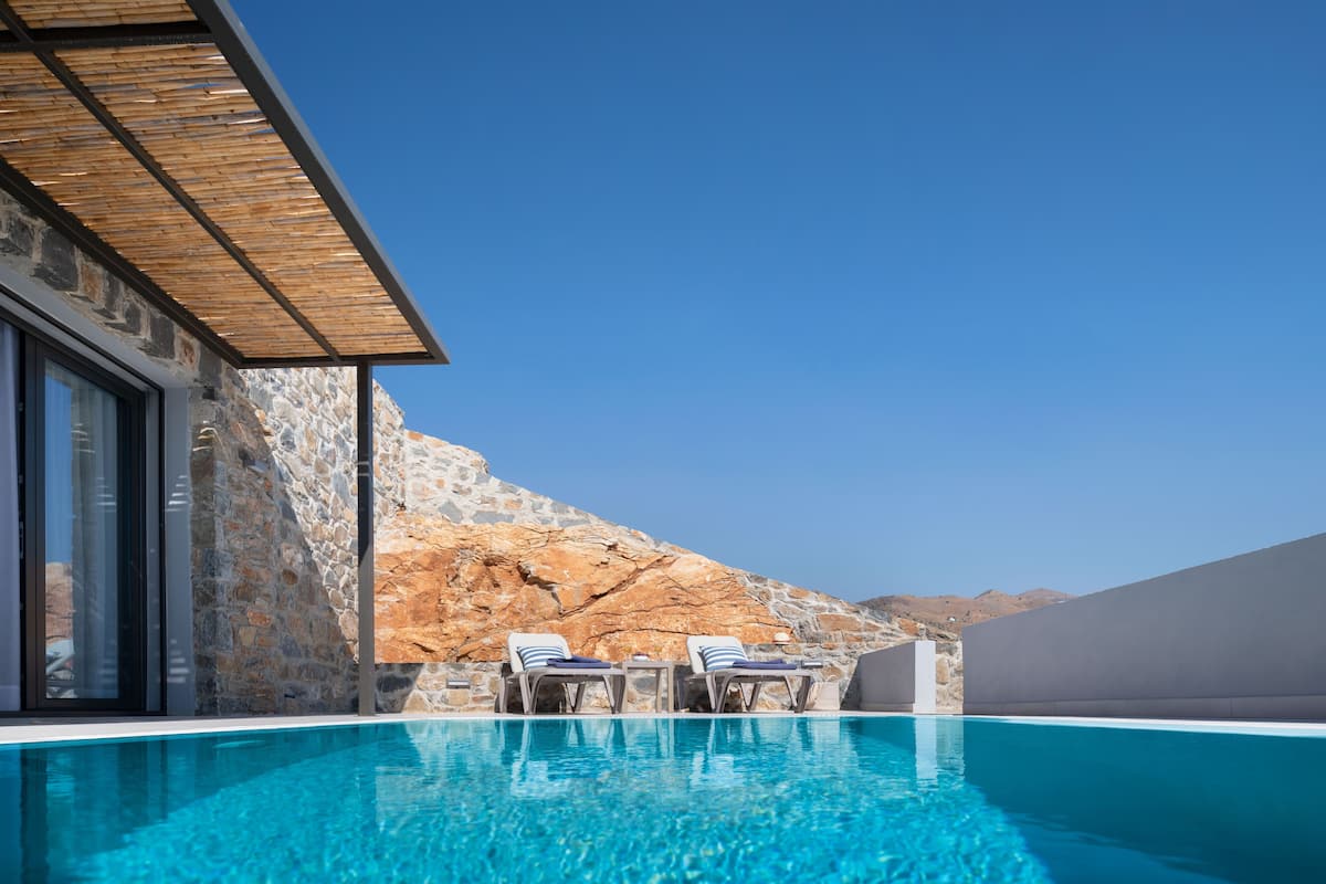Una piscina con sillas de descanso, un muro de piedra y un cielo azul despejado.