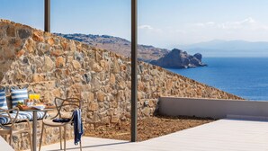 Un mur de pierre avec une table et des chaises, une pergola en bois et une vue sur la mer.