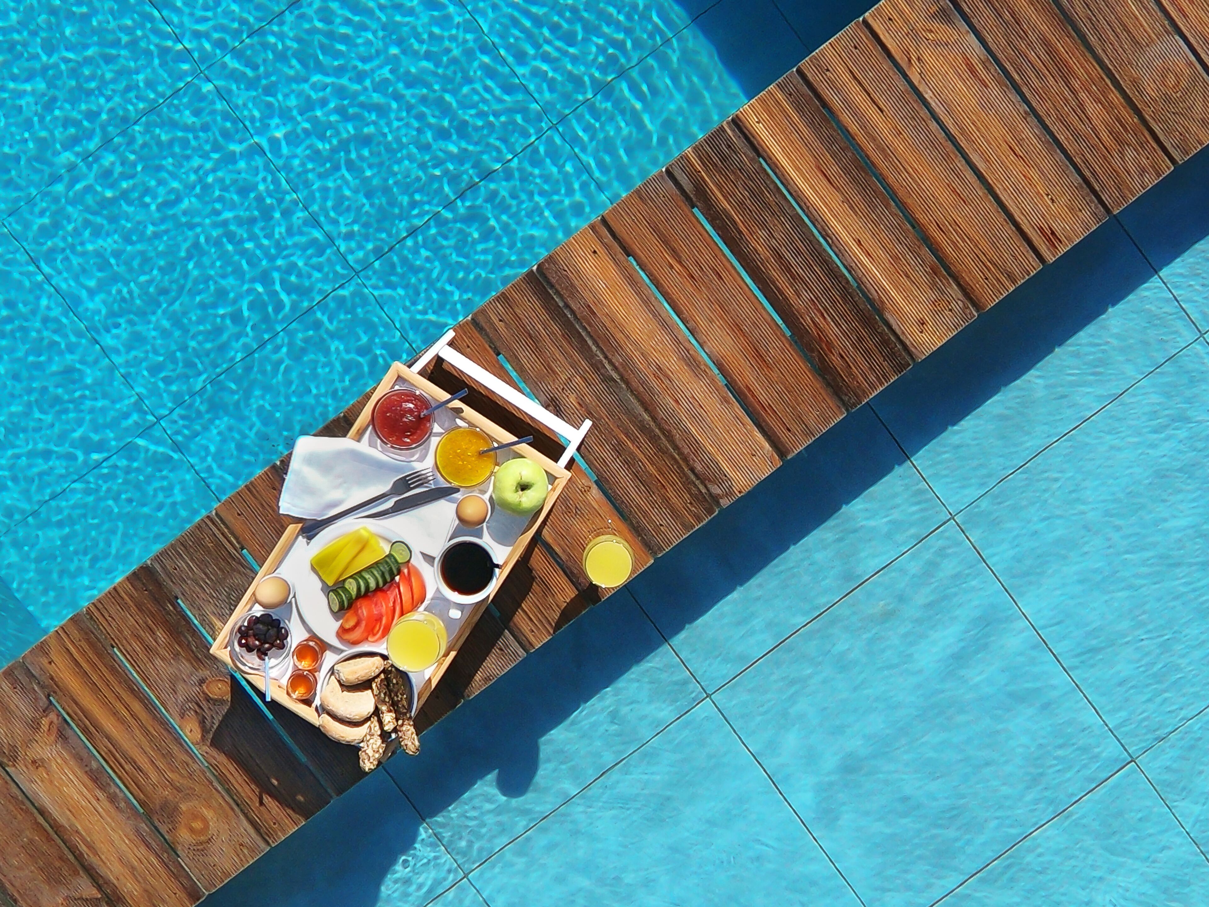 Una terraza de madera sobre una piscina, con una bandeja de comida y bebidas.