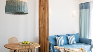 Un salon moderne avec une table à manger en bois, des chaises en osier, un canapé bleu agrémenté de coussins à rayures et un luminaire suspendu.