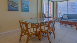 Un coin repas avec une table en verre et des chaises en bois, deux tableaux accrochés au mur et une vue sur les bâtiments à travers de grandes fenêtres.
