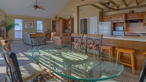 A spacious living area with a glass dining table, wooden chairs, and a ceiling fan. - Kokomo by Meyer Vacation Rentals (Gulf Shores)