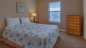 A bedroom with a bed, a nightstand, a dresser, a ceiling fan, a window with blinds, and a framed picture on the wall. - Kokomo by Meyer Vacation Rentals (Gulf Shores)