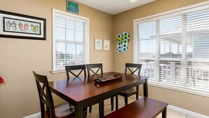A dining area with a wooden table and four chairs, large windows with blinds, and a ceiling fan. - Red Robyn by Meyer Vacation Rentals (Gulf Shores)