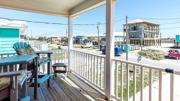 A wooden deck with outdoor furniture, a view of a beach, and a building under construction. - Red Robyn by Meyer Vacation Rentals (Gulf Shores)