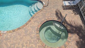 Une piscine avec une plage en briques et un petit jacuzzi.