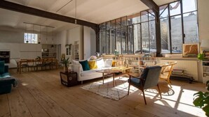 A spacious living area with a large window, wooden flooring, a white sofa, and a dining table. - La Fleur Loft Boutique Spa (Villa General Belgrano)