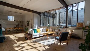 A spacious living room with a wooden floor, a white sofa with yellow cushions, a wooden coffee table, and a large window providing natural light. - La Fleur Loft Boutique Spa (Villa General Belgrano)