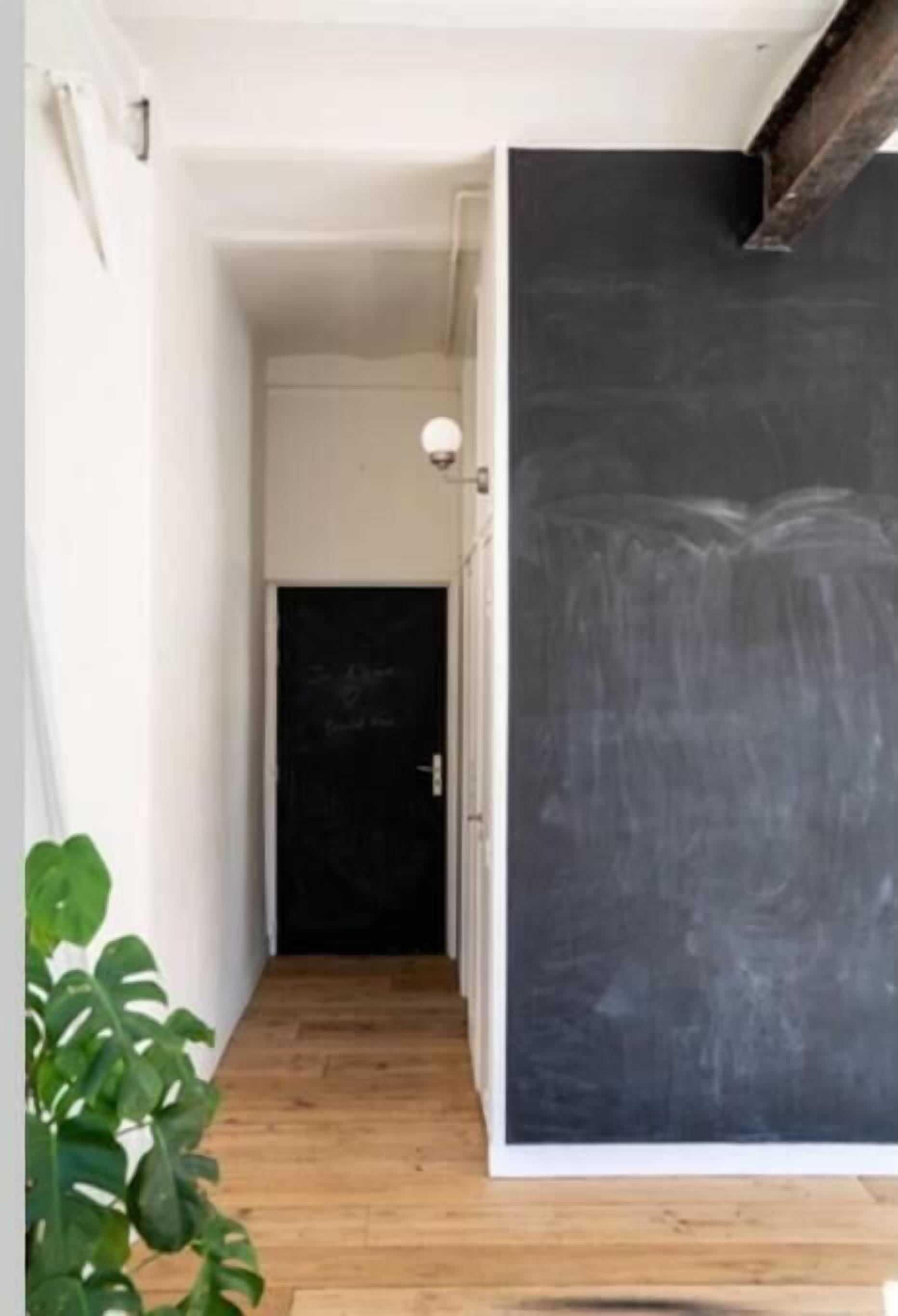 A hallway with a large blackboard on the right, a wooden floor, and a door at the end.