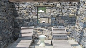 Una habitación con paredes de piedra, dos sillones de madera y una mesa blanca sobre pedestal.