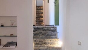 Una escalera de piedra conduce a un piso superior, un estante de cristal con adornos, y un marco de puerta verde.